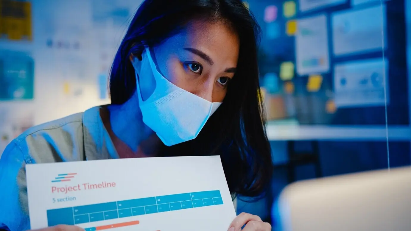 Una empresaria asiática practica el distanciamiento social en la nueva normalidad como medida de prevención mientras, en la oficina por la noche, usa un portátil para presentar a sus colegas un plan por videollamada. La vida después del coronavirus.