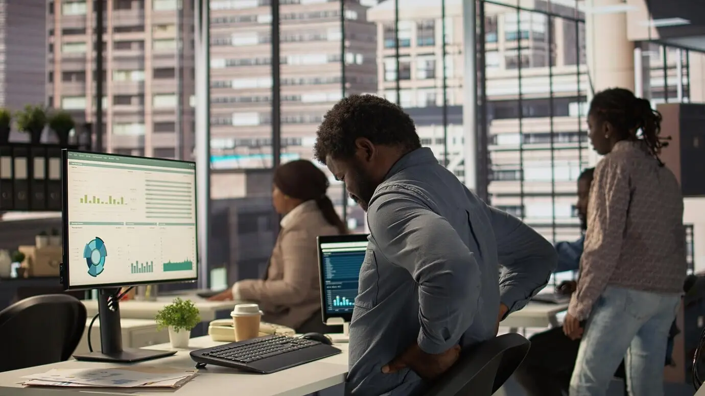 Un empleado afroamericano de una empresa hace una pausa para estirar su espalda en la oficina.