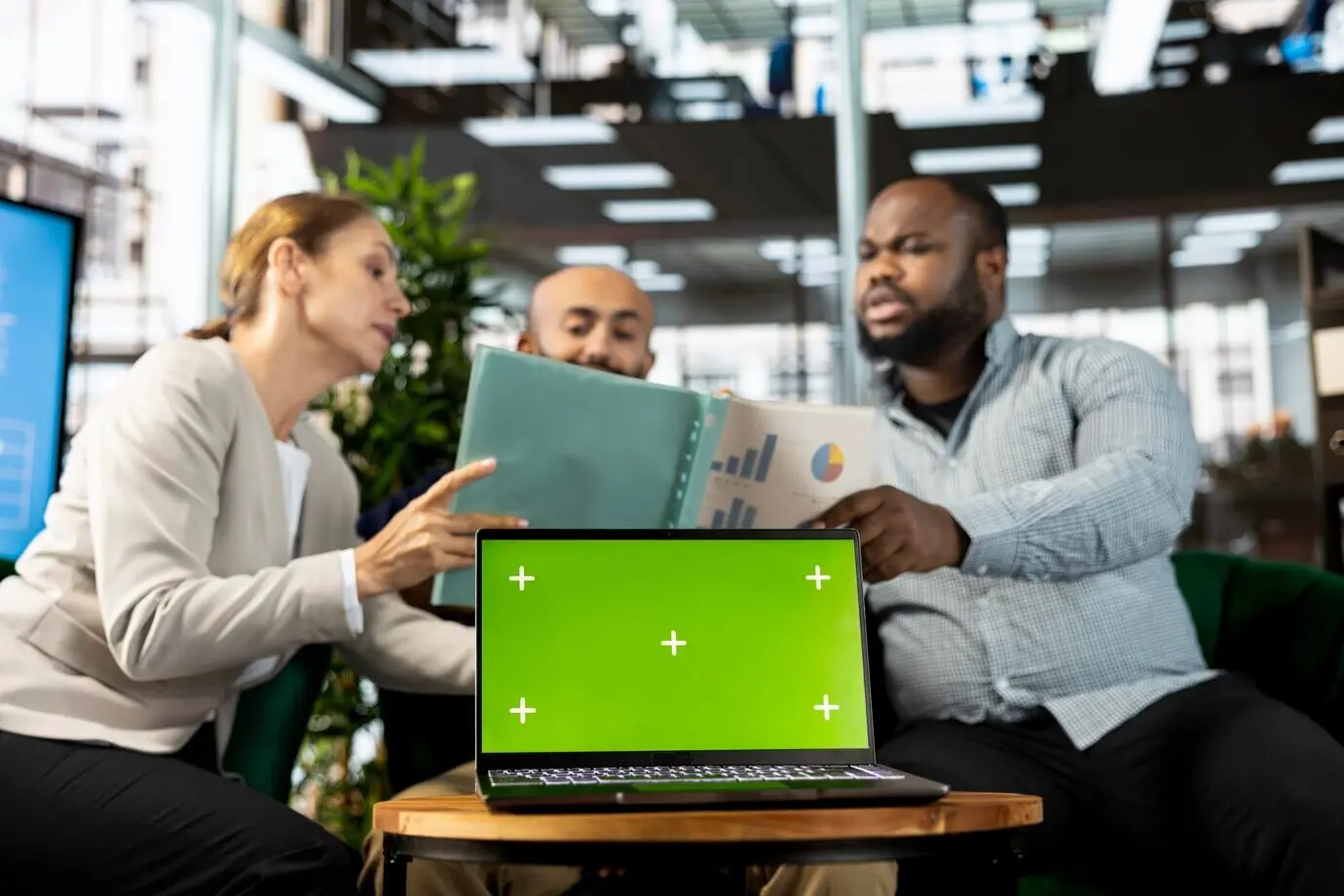 Portátil con clave de croma junto a empleados de oficina que leen estadísticas de datos.